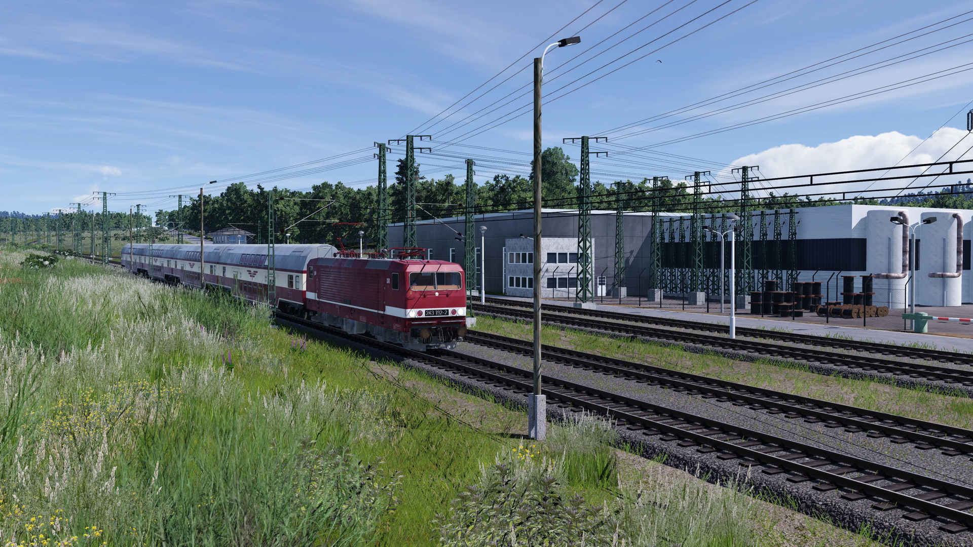Eine BR 243 fährt mit ihrem Doppelstockzug am Bahnstromwerk vorbei.