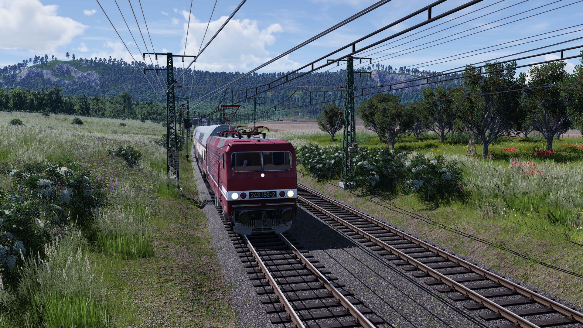 Eine BR 243 durchfährt mit ihrem Doppelstockzug in Sputniklackierung die Landschaft.