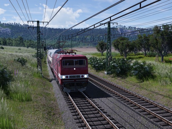 Eine BR 243 durchfährt mit ihrem Doppelstockzug in Sputniklackierung die Landschaft.
