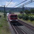 Eine BR 243 durchfährt mit ihrem Doppelstockzug in Sputniklackierung die Landschaft.